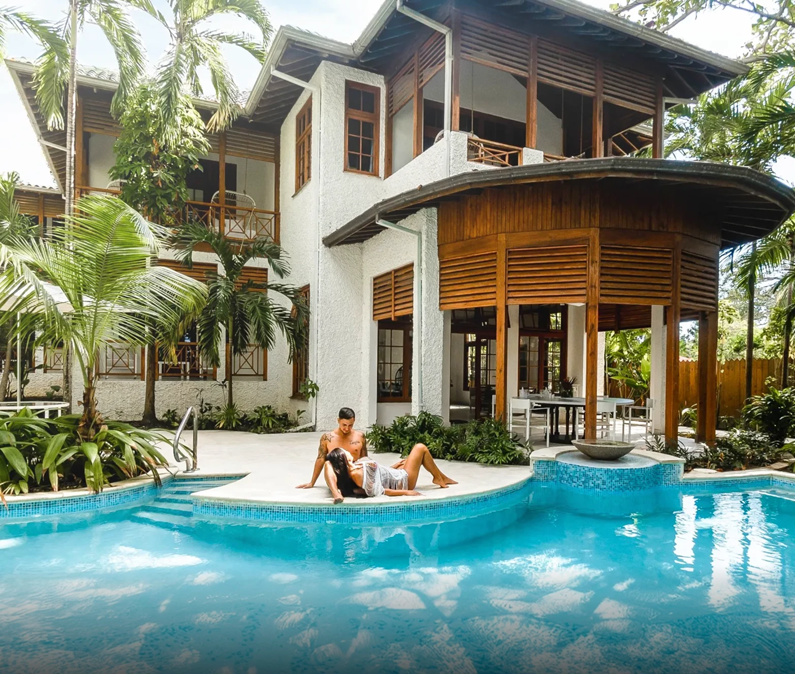 two men sitting on the edge of a pool in front of a house