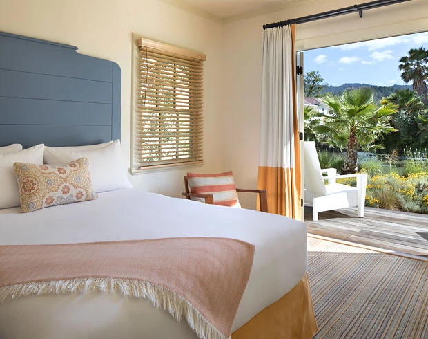 guest room with white sheets, orange accents colors, blue headboard, and a sliding glass door open leading to an walkout outdoor terrace
