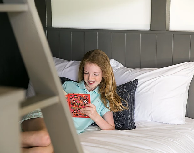a young girl sitting on the bottom bunk bed reading a book