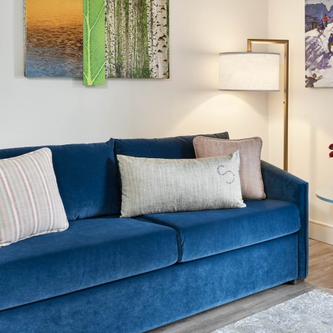 a blue couch with pillows in a room with a lamp and pictures on the wall