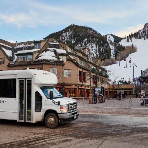 a white bus on a street with buildings and snow covered mountains