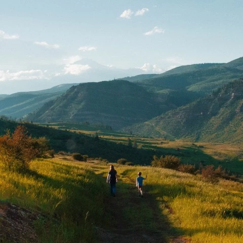 two people walking on a path in a grassy valley