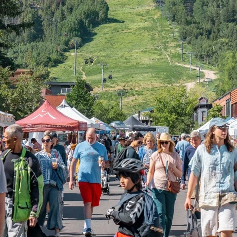 a group of people walking down a street with tents and trees