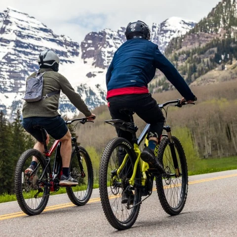 two people riding bicycles on a road with mountains in the background
