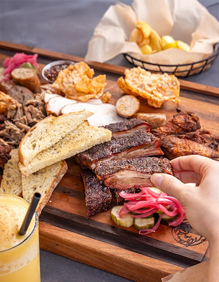 a hand holding a piece of meat with pickles and a glass of juice