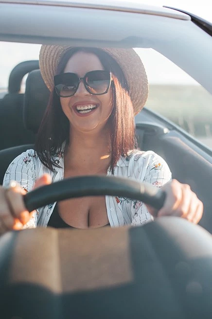 woman smiling with 2 hands on the wheel