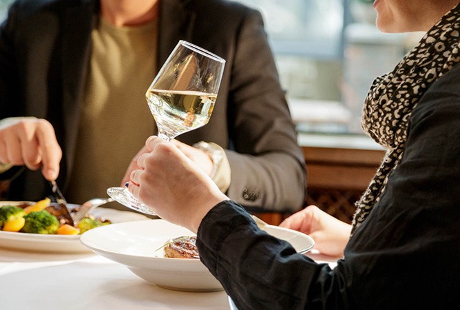 woman holding white wine while eating