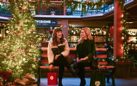 two women sitting on a bench in front of a christmas tree