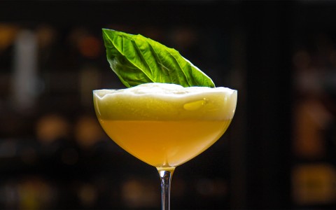 a glass with a yellow liquid and a green leaf on top