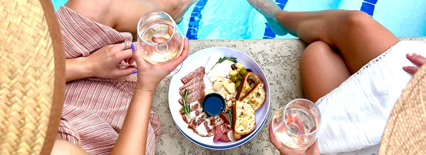 a plate of food with wine and a person holding wine glasses