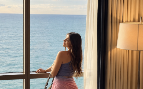 a woman standing in front of a window overlooking the ocean