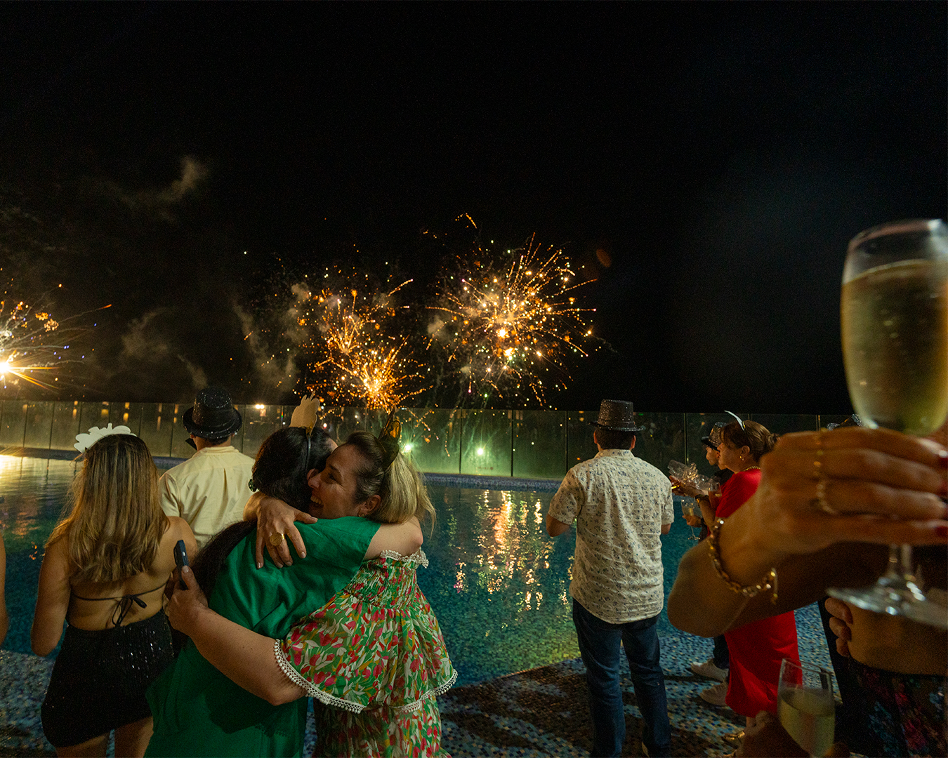 a group of people hugging by a pool with fireworks