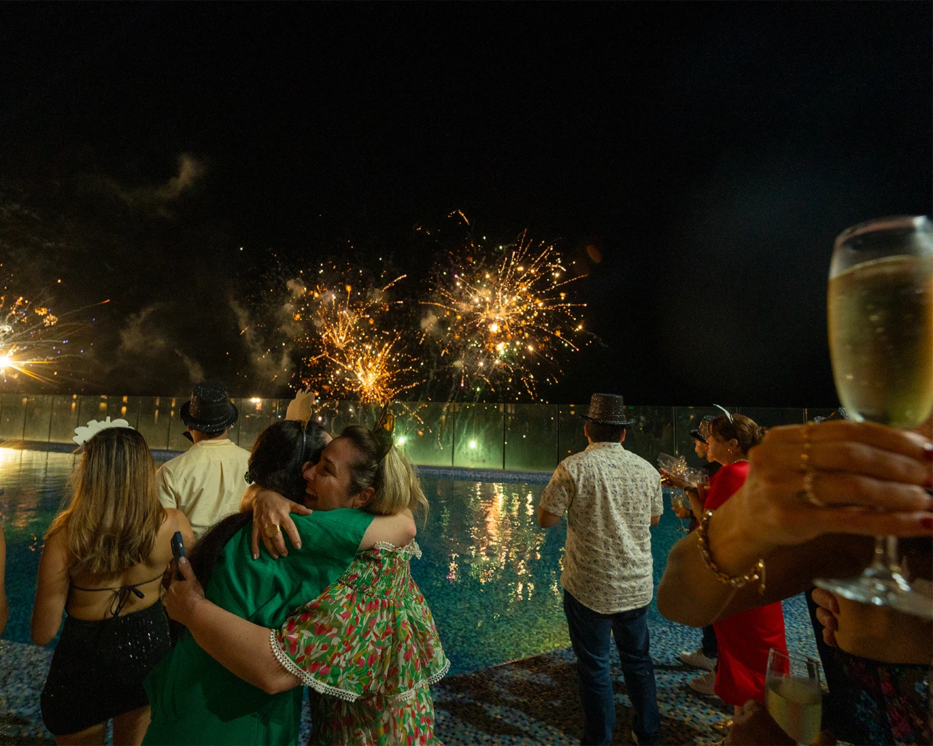 a group of people hugging by a pool with fireworks