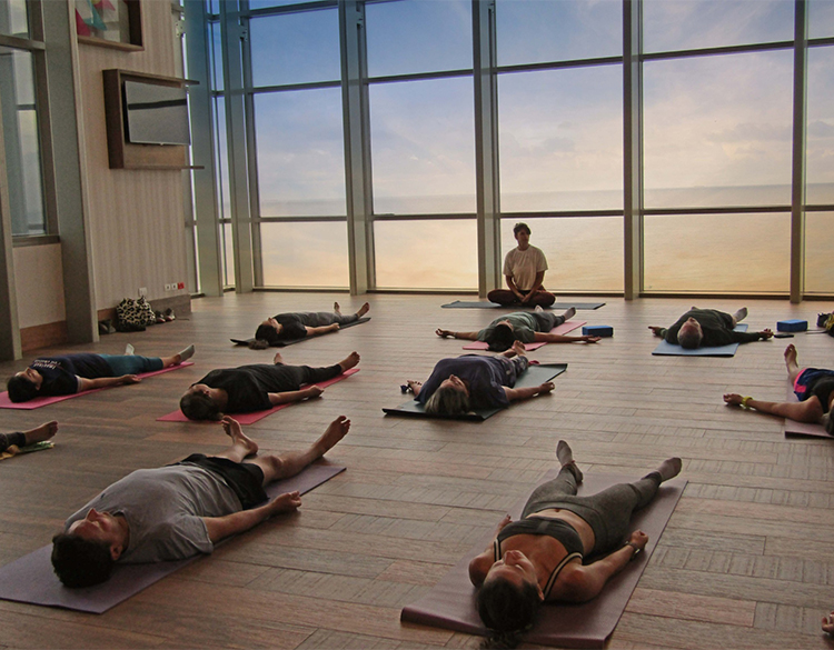a group of people lying on mats in a room with large windows