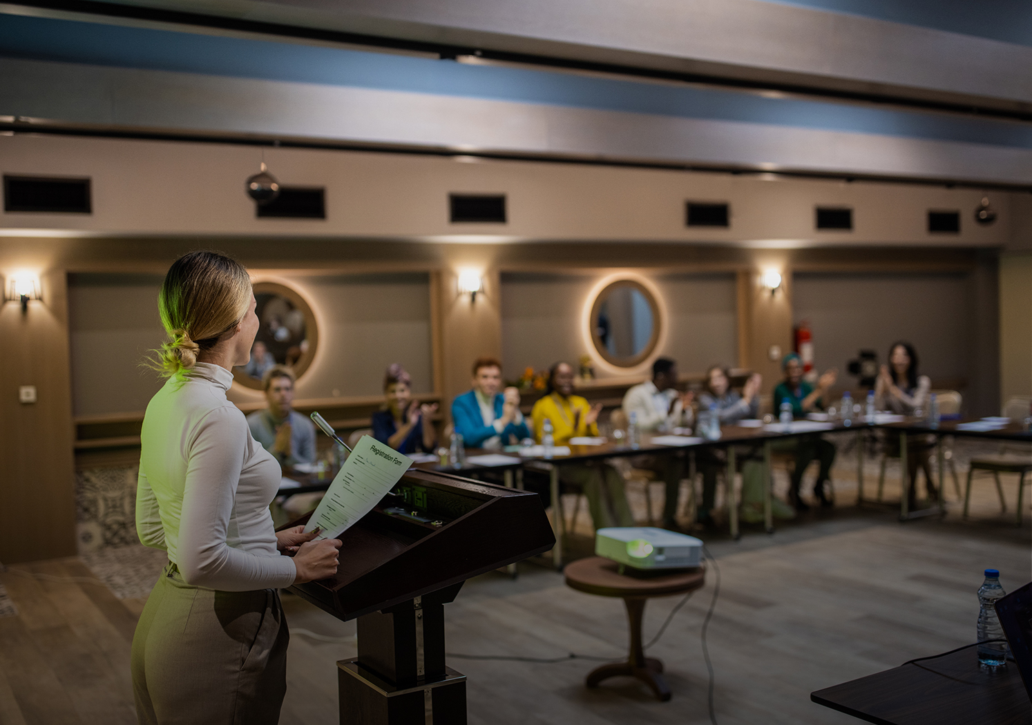 a woman standing at a podium with a microphone and people in the background