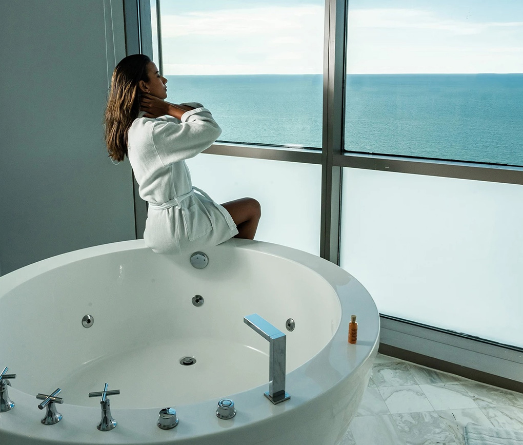 a woman sitting on a bathtub looking out a window