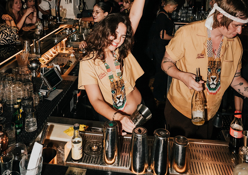 a woman holding a shaker and smiling at a bar