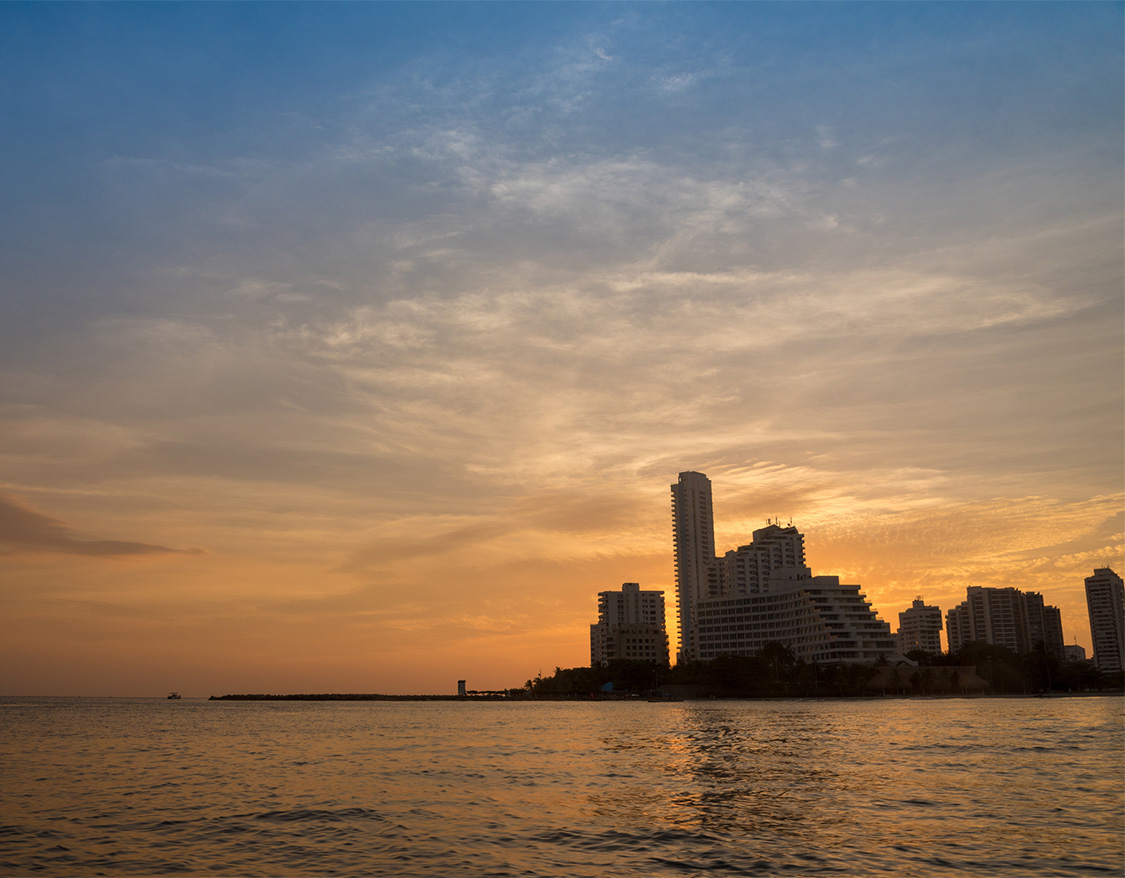 a city skyline with a body of water and a sunset