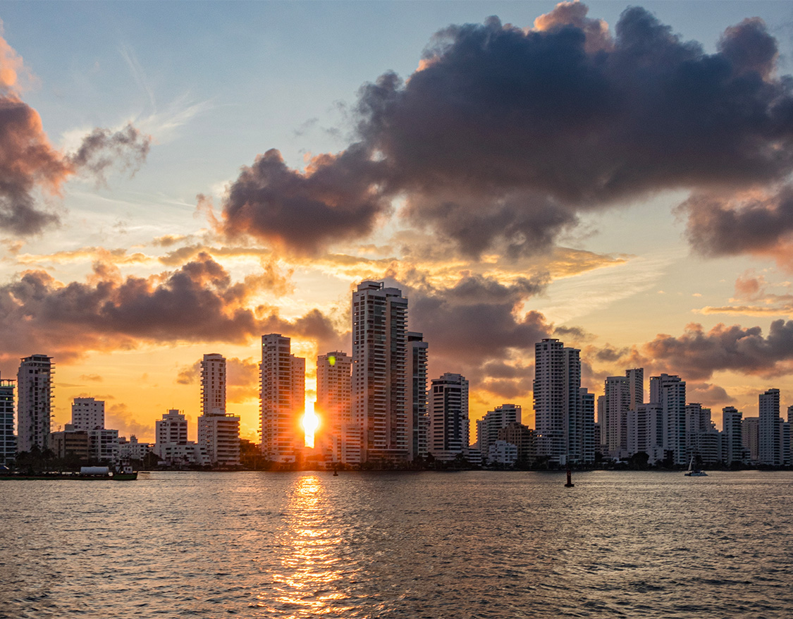 a city skyline with a body of water and a sunset