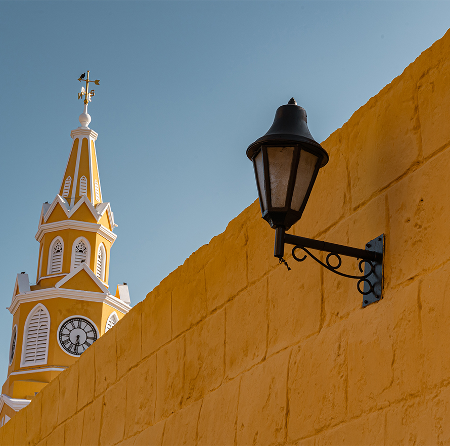 a yellow building with a clock tower and a lamp on a wall