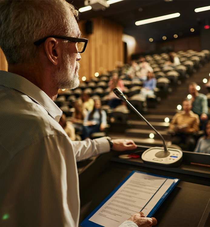 a man standing at a podium with a microphone and a clipboard