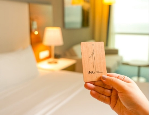 a hand holding a wooden card in front of a bed