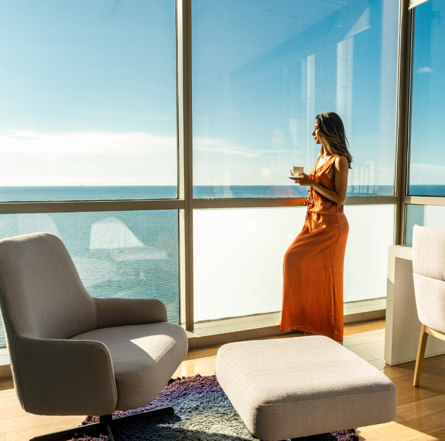a woman in a dress holding a cup and standing by a window