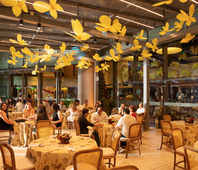 a group of people sitting at tables in a room with yellow flowers from ceiling