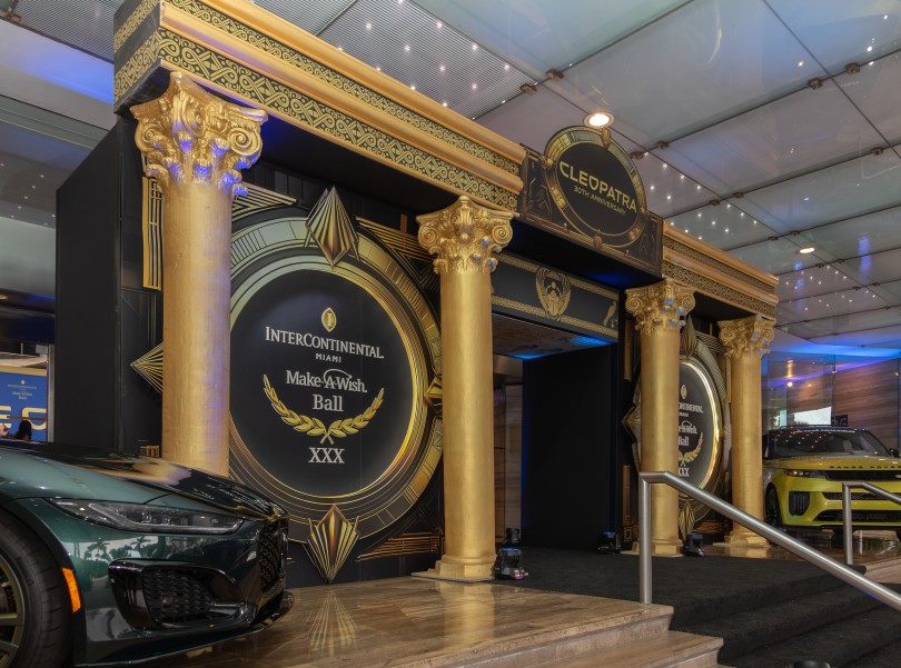 a black and gold entrance with columns and a car parked in front