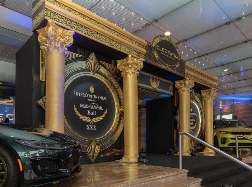 a black and gold entrance with columns and a car parked in front