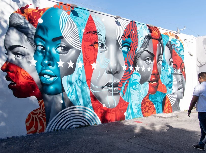 a man standing in front of a wall with a mural of women