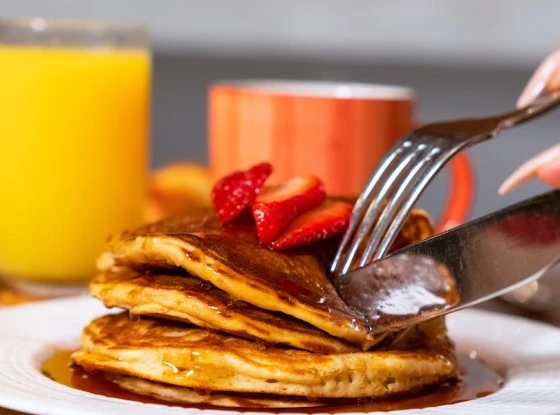 a fork and knife on a stack of pancakes with syrup