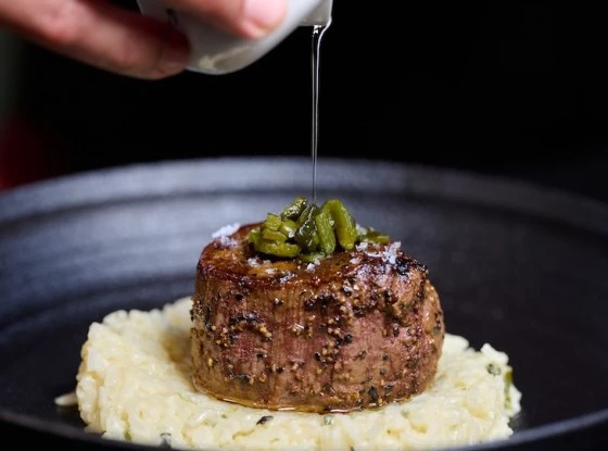 a person pouring a sauce onto a piece of meat