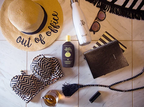A flat lay image of travel accessories, sunglasses, sunscreen, hat
