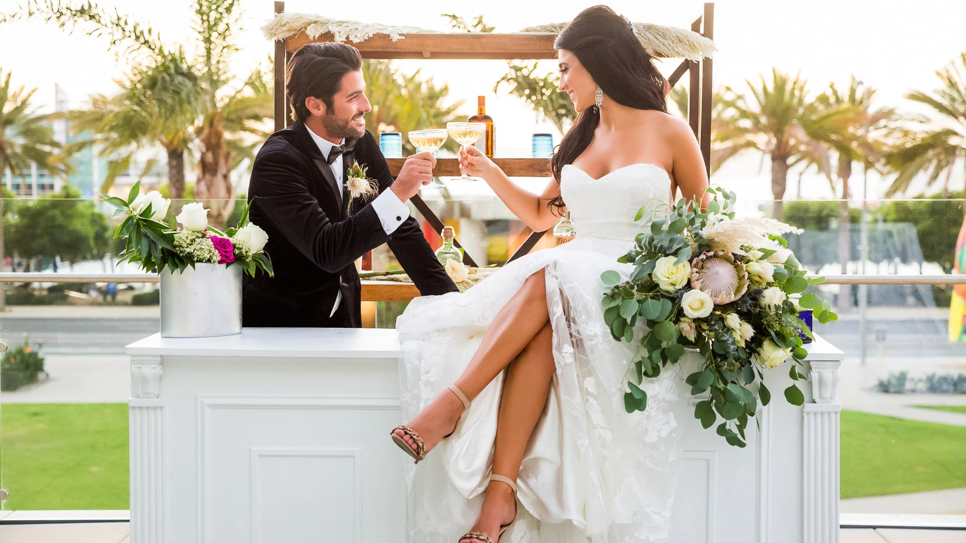 a man and woman sitting on a ledge holding wine glasses