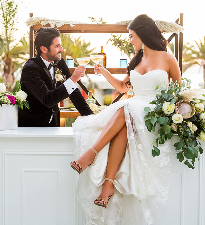 a man and woman sitting on a ledge holding wine glasses