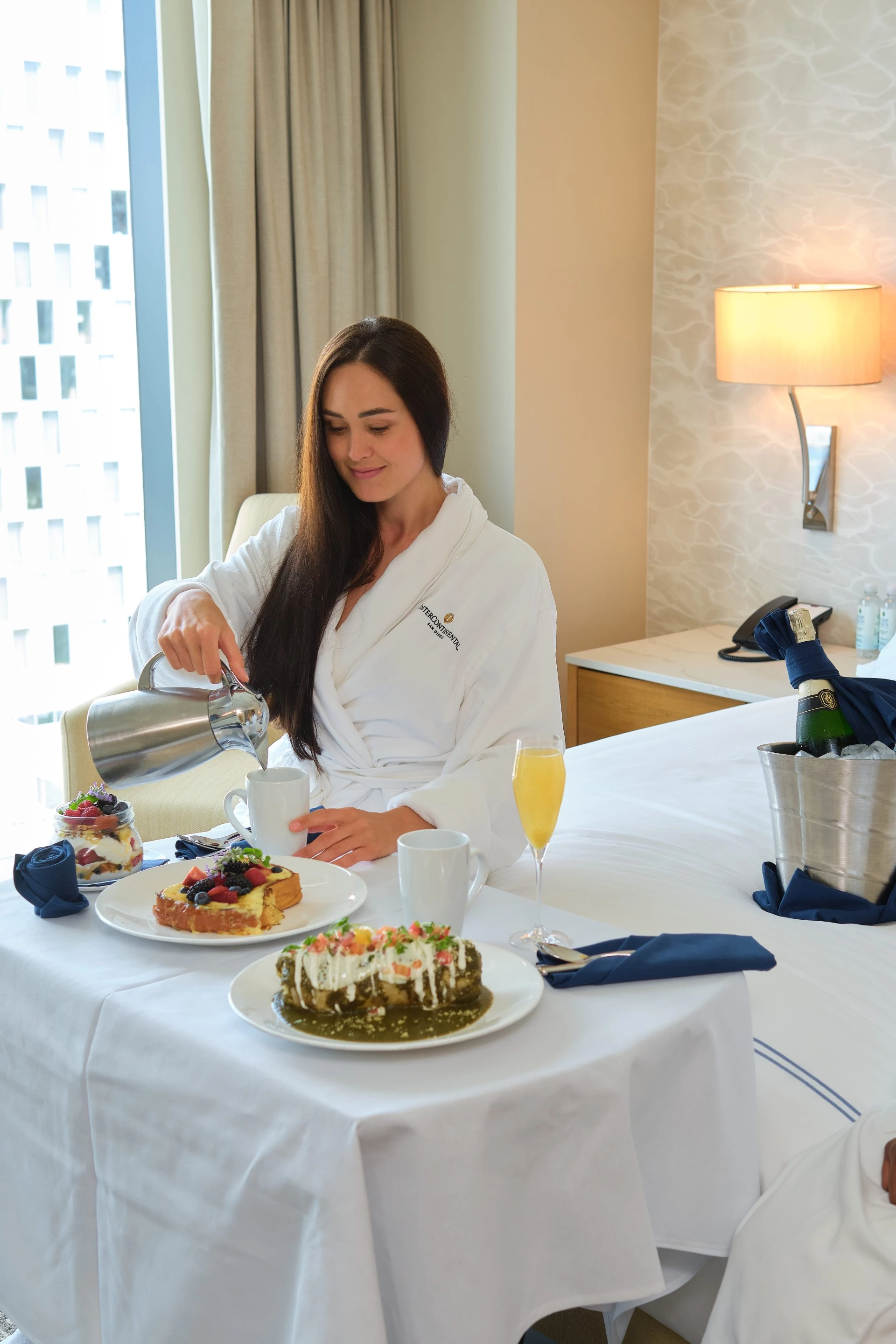a woman in a white robe sitting at a table with food on it