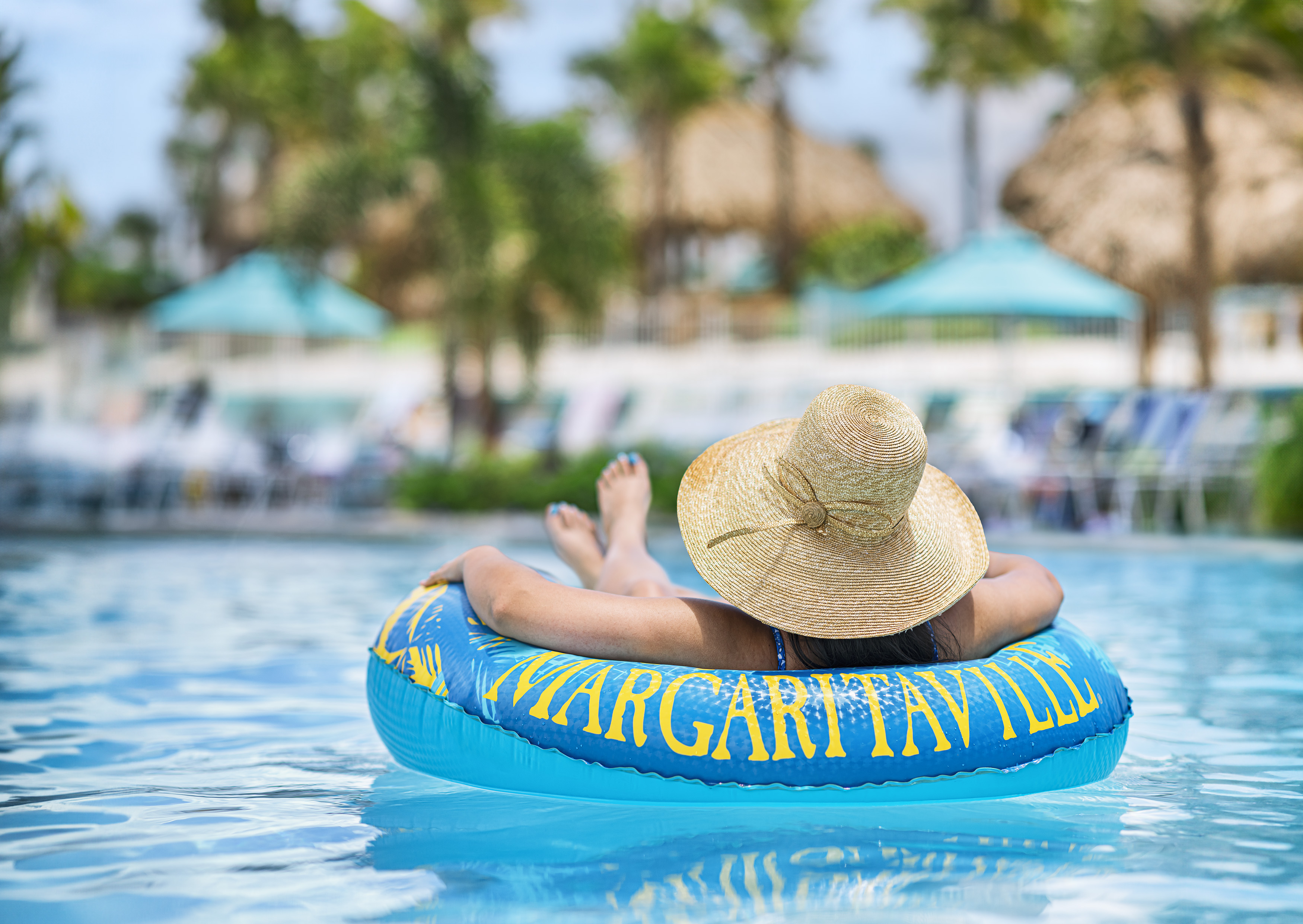 a woman in a pool wearing a hat and lying on a blue inner tube