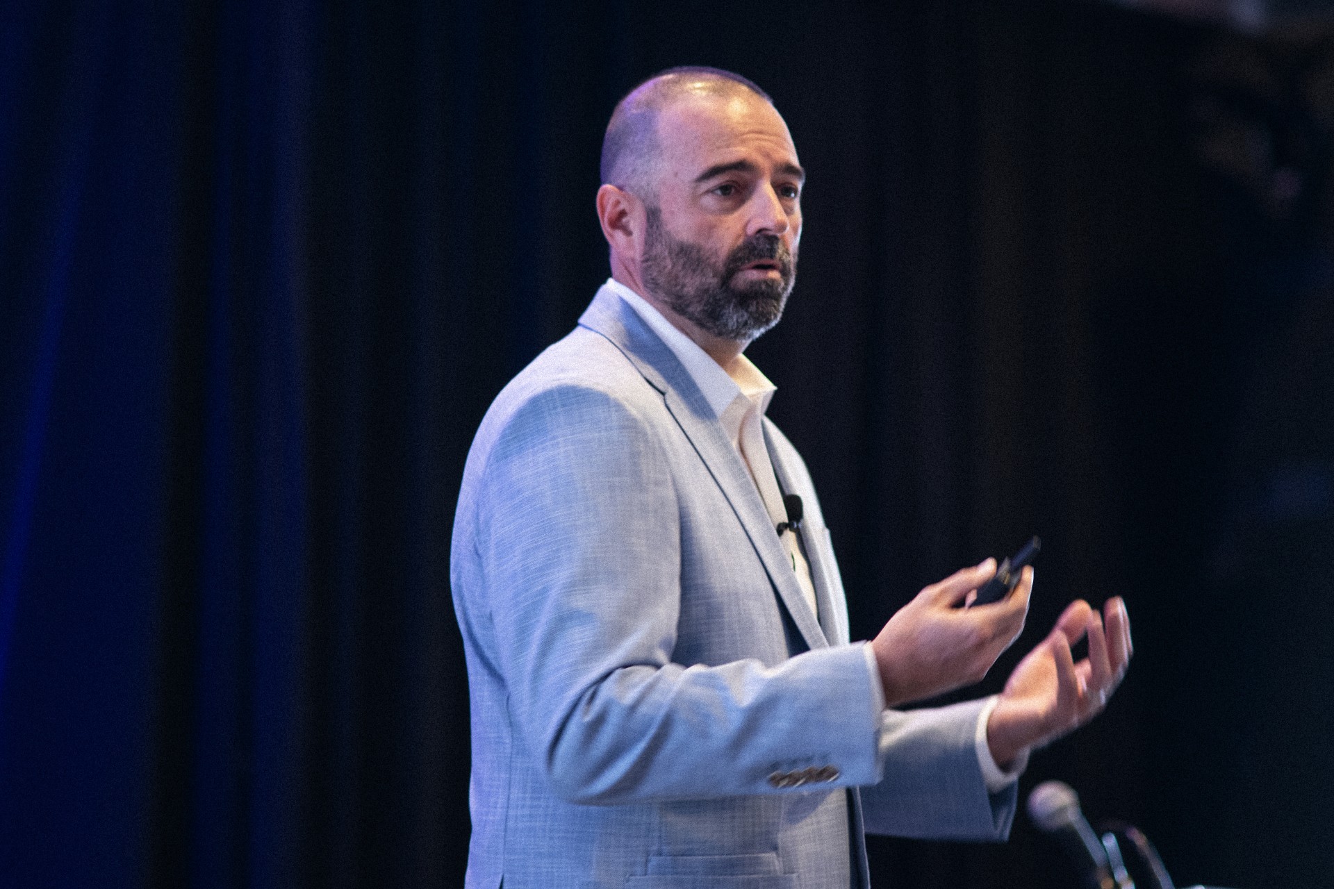 Gregg Forde in a suit standing in front of microphones