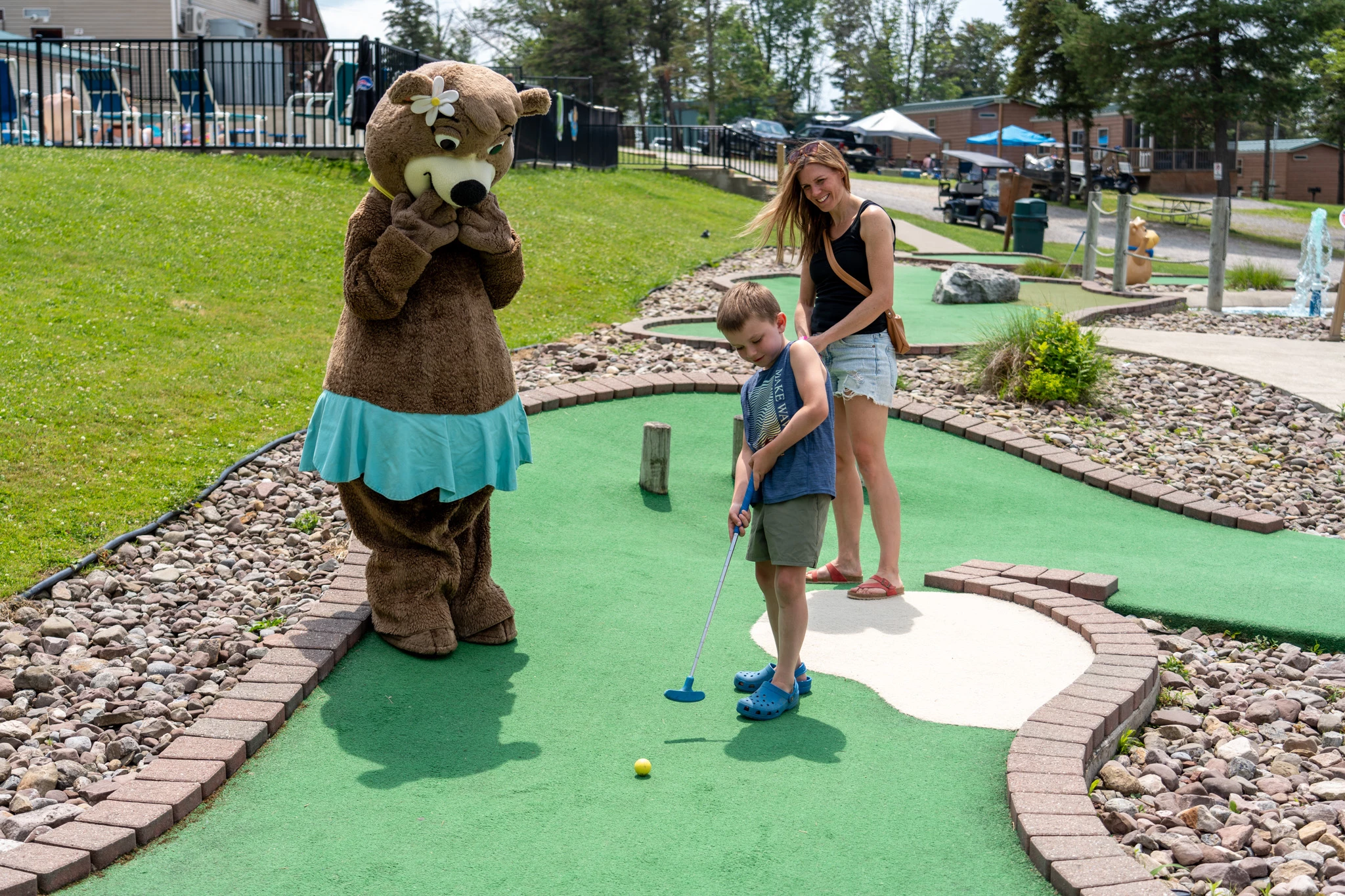 a child playing golf with a person in a bear garment