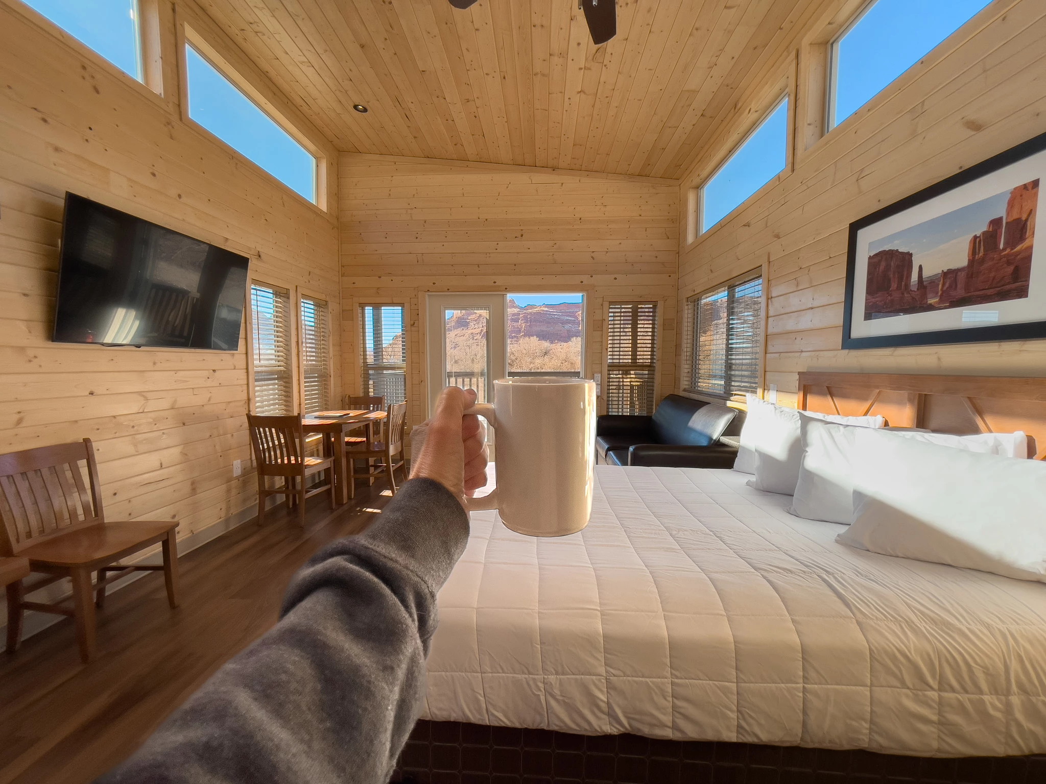 a hand holding a mug in a room with a bed and a window