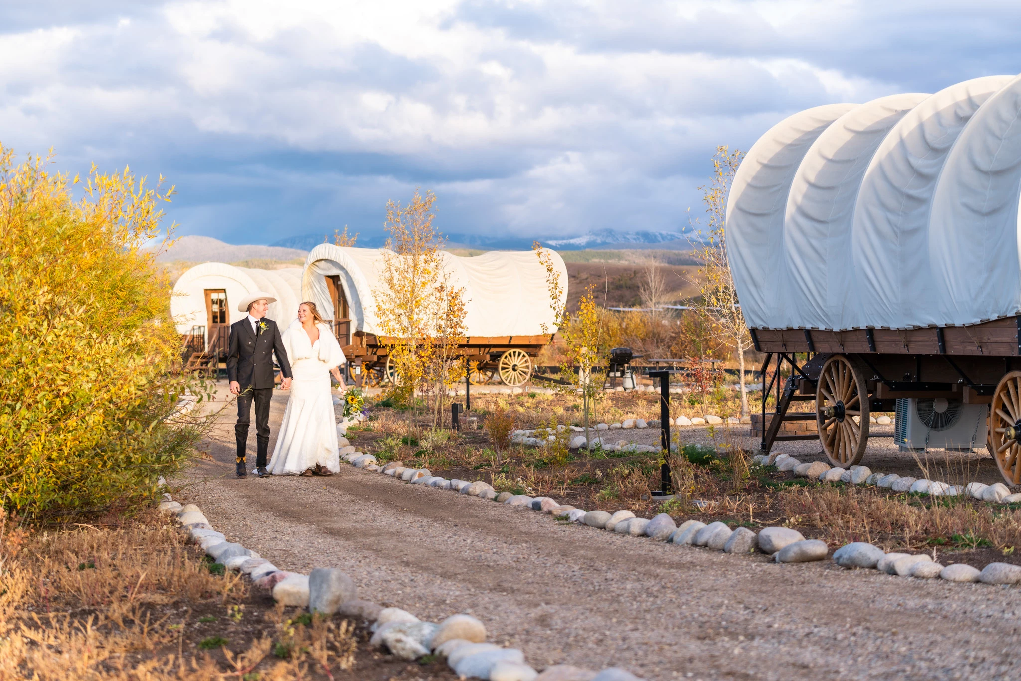 a man and woman walking on a path with covered wagon