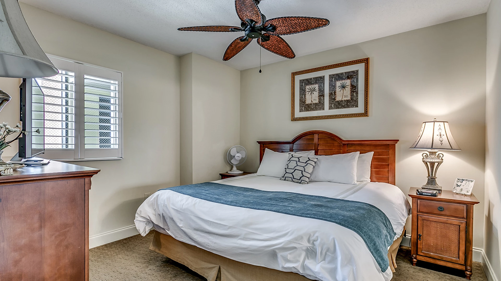 A hotel room with a bed, nightstand, dresser, ceiling fan, and window.