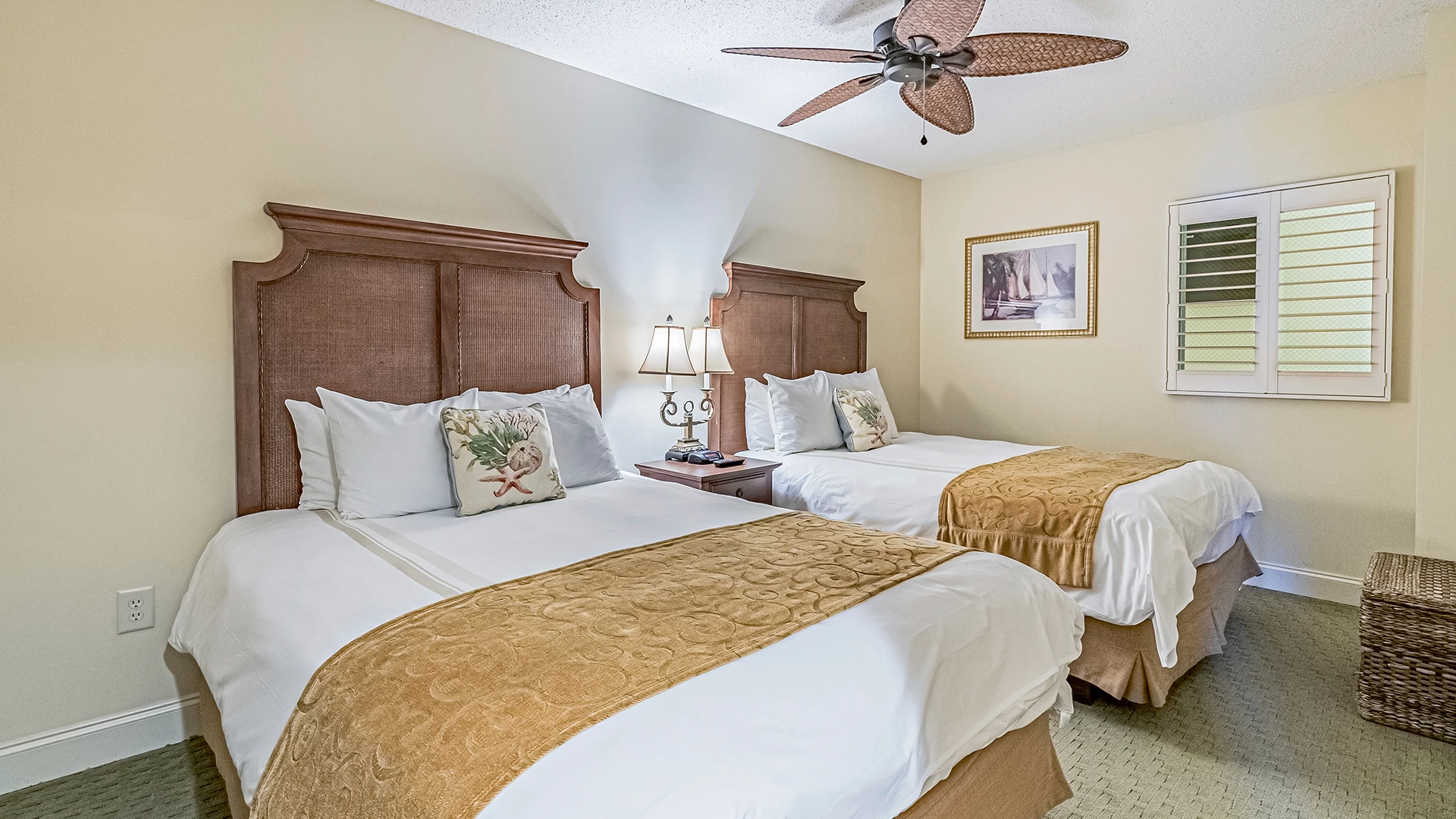 A hotel room with two twin beds, wooden headboards, and white bedding with gold runners.