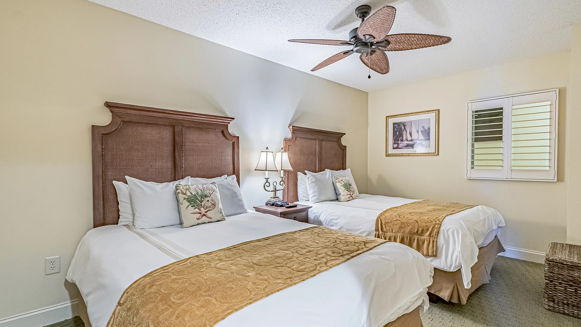 A hotel room with two twin beds, a ceiling fan, nightstand, lamp, and window.