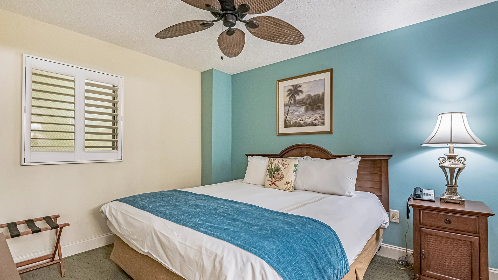 A hotel room with a bed, nightstand, lamp, ceiling fan, and window
