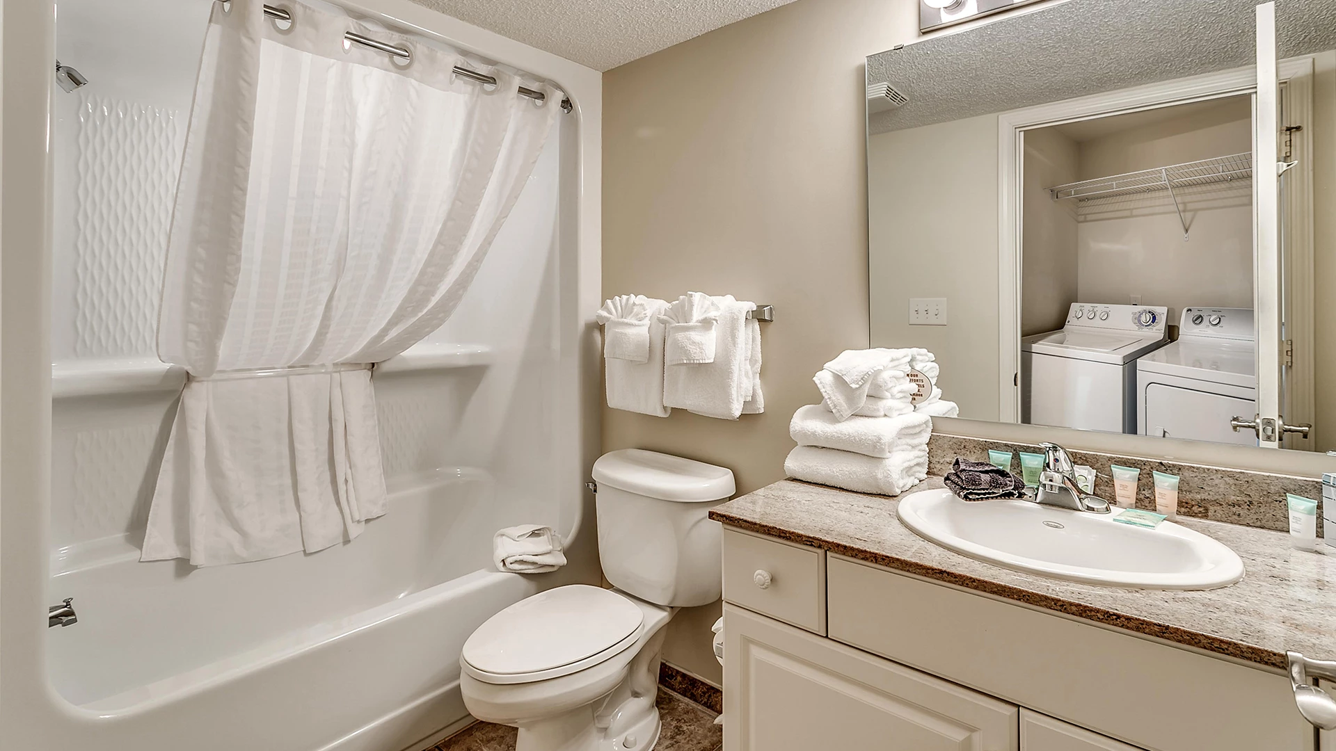 A clean bathroom with a bathtub, toilet, sink, and stacked towels.