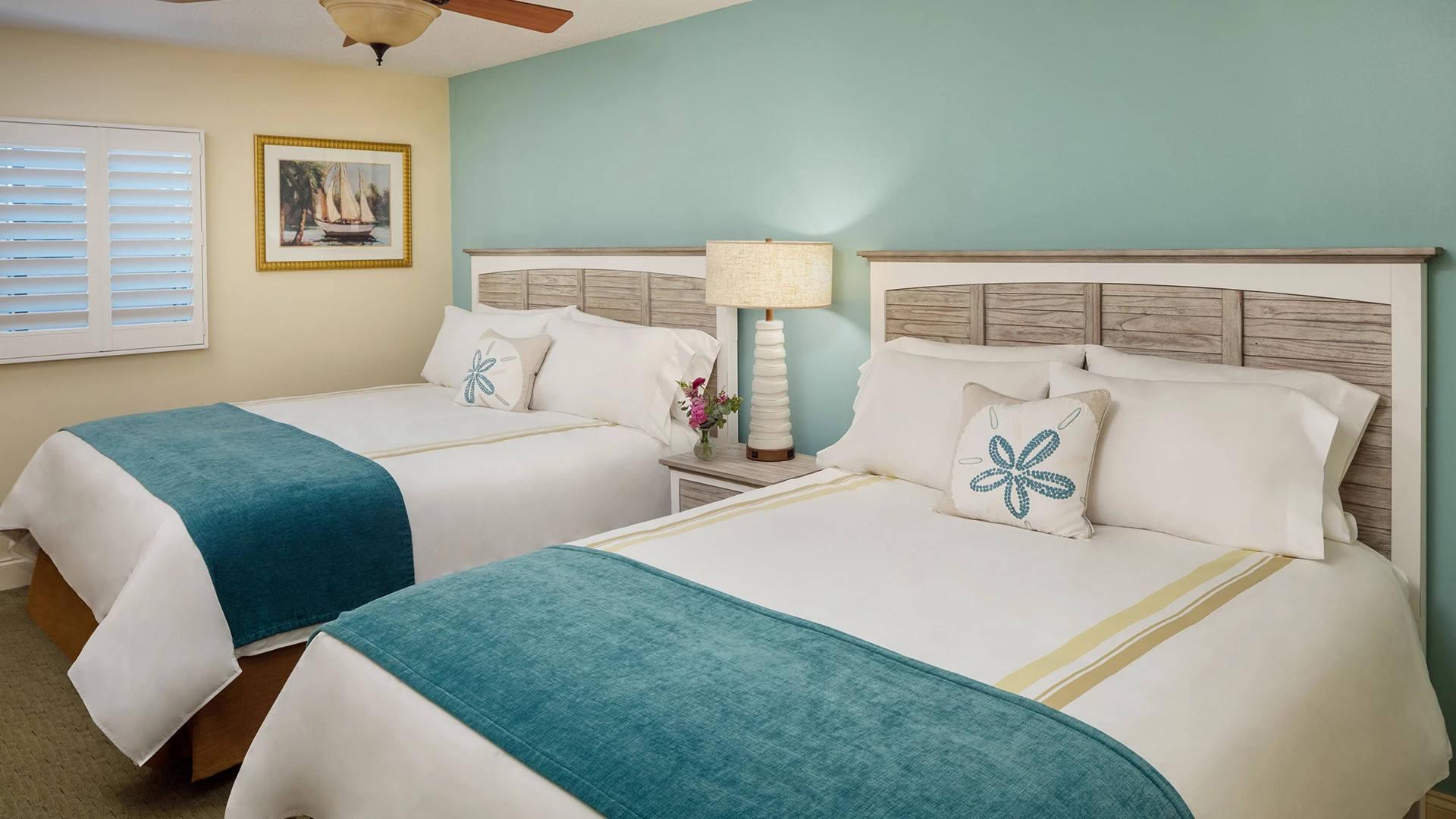 A hotel room with two beds, a nightstand, a lamp, and a window
