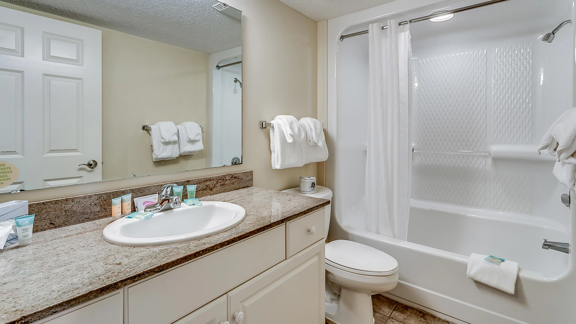 A clean bathroom with a granite countertop, white sink, toilet, bathtub, and mirror.