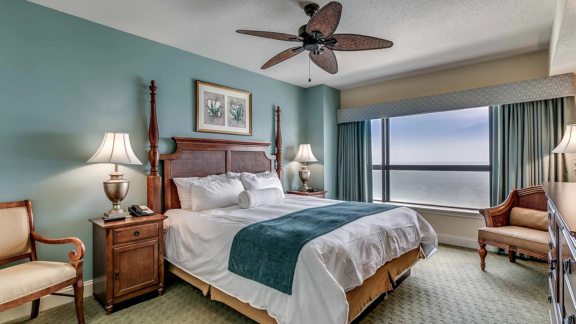 A hotel room with a large bed, two nightstands, a chair, and a window with an ocean view.